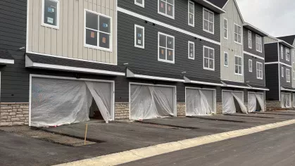 Three-story townhome buildings with gray and beige siding, covered garage openings, and new pavement throughout the developing apartment community.
