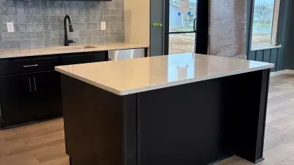 Community kitchen with a large black island, blue tile accent wall, floating shelves, and a modern light fixture next to floor-to-ceiling windows.