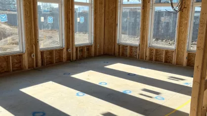 Sunlight streaming through large windows onto the concrete floor of a townhome unit during the interior framing phase.