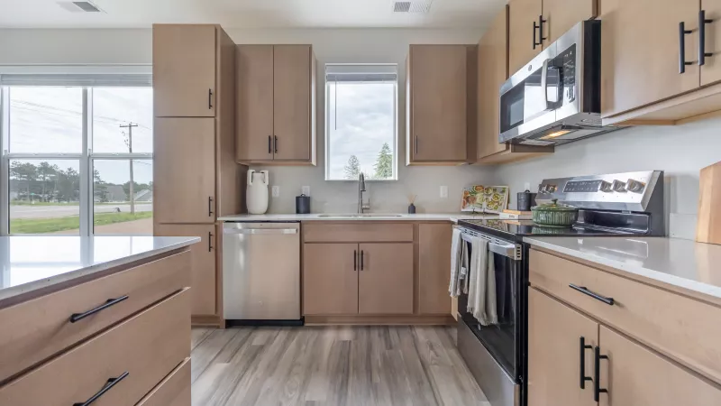 Modern kitchen with light wood cabinets, stainless steel appliances, white countertops, and wood-look flooring.