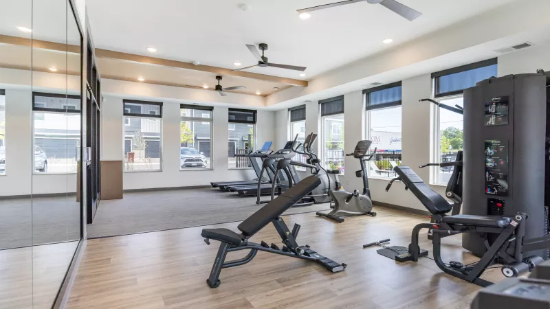 Bright gym with a weight bench, treadmills, exercise bikes, and a large mirror.