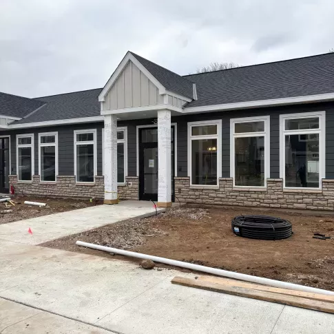 Modern commercial building exterior with dark gray siding, white trim, stone wainscoting, and covered entrance during construction