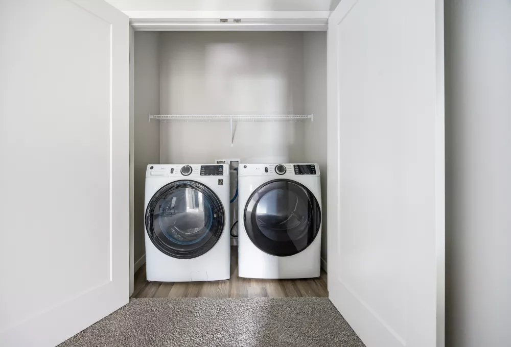 Two white front-loading washer and dryer machines in a bright, minimalist closet with a shelf above.