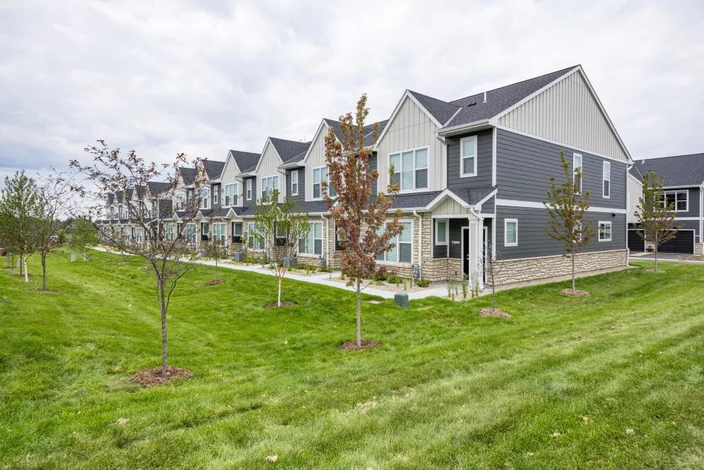 Row of modern townhouses with dark gray siding, light gables, and stone accents, set against a green lawn and cloudy sky.