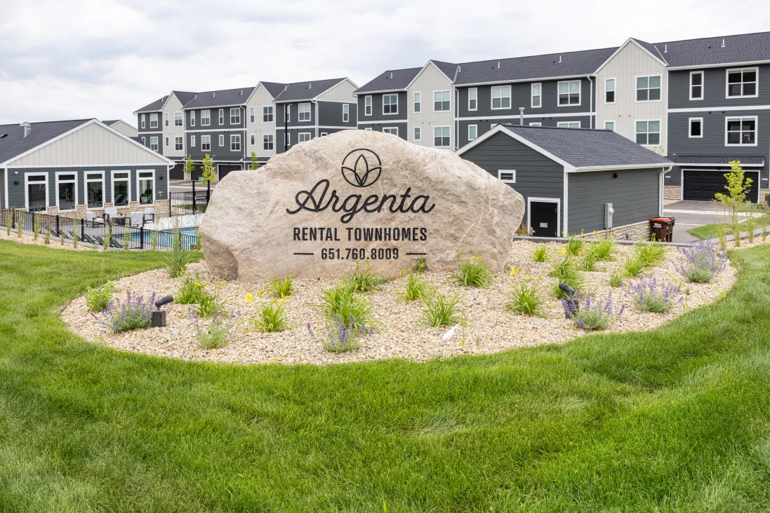 Large rock sign for Argenta Rental Townhomes, with modern apartment buildings and a pool behind it.