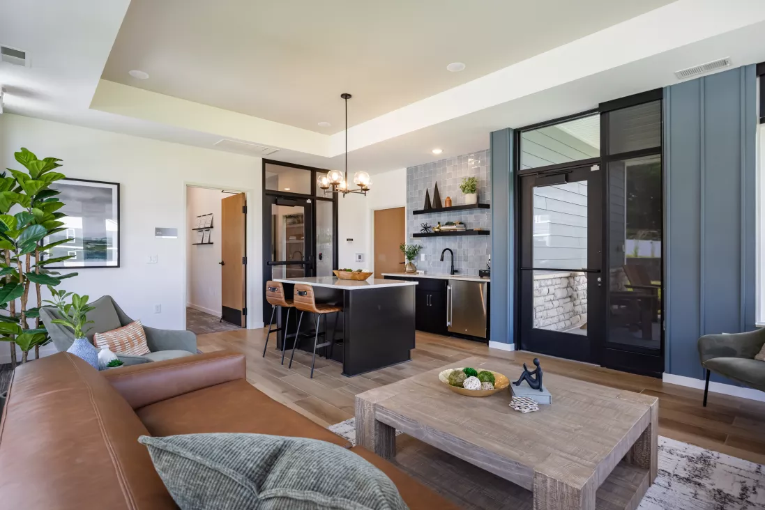 Stylish open-concept living space with a brown sofa, wood coffee table, and a modern kitchen island with dark cabinetry. Light wood floor.