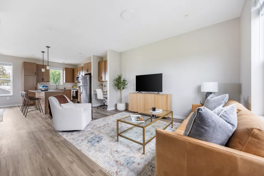 Bright, modern open-concept living room with a brown leather sofa, light wood media console, and an adjacent kitchen area.